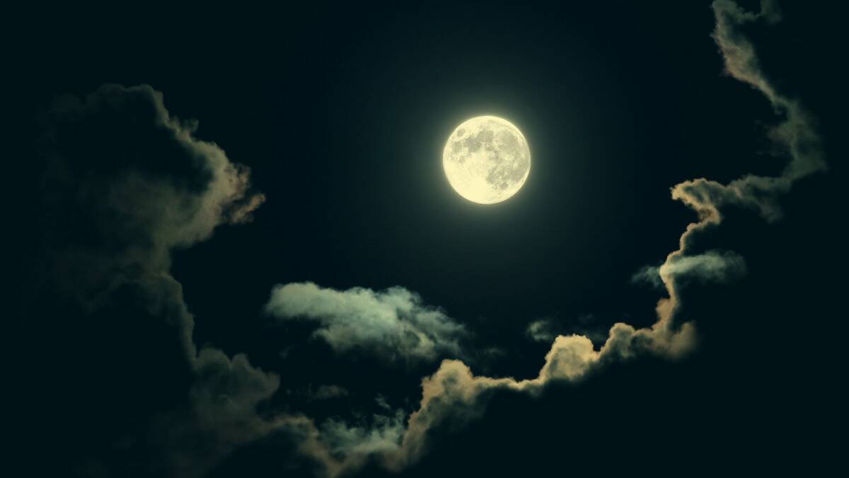 The full moon in the sky, clouds surrounding it.