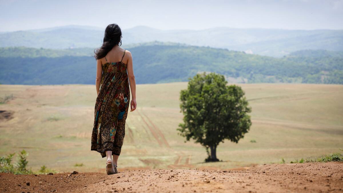 A woman walking away from the camera toward a large field.