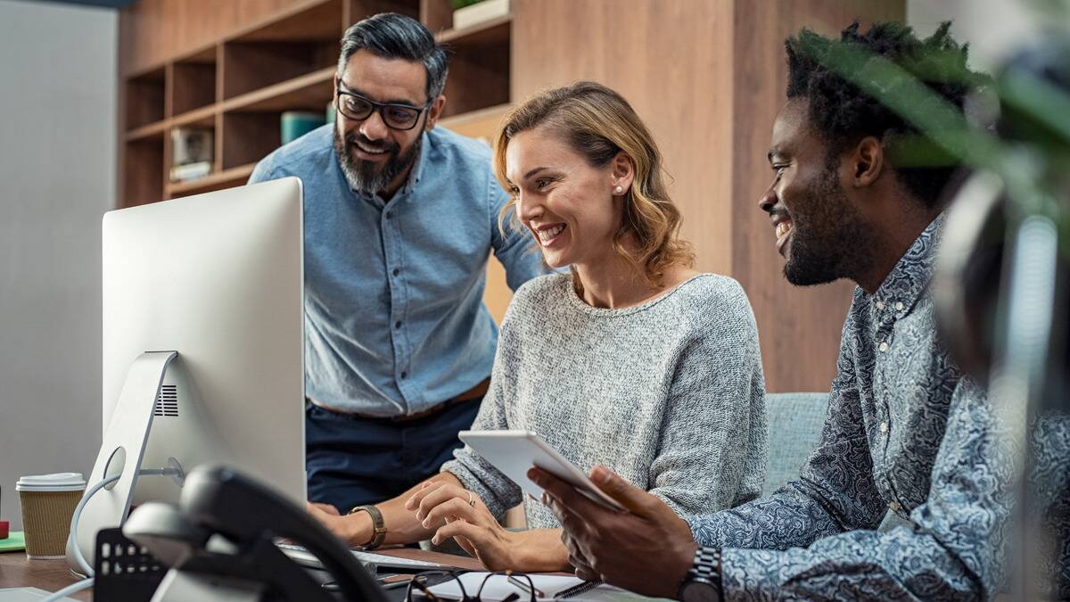 Three people sitting in front of a computer at work, all smiling as they check something out.