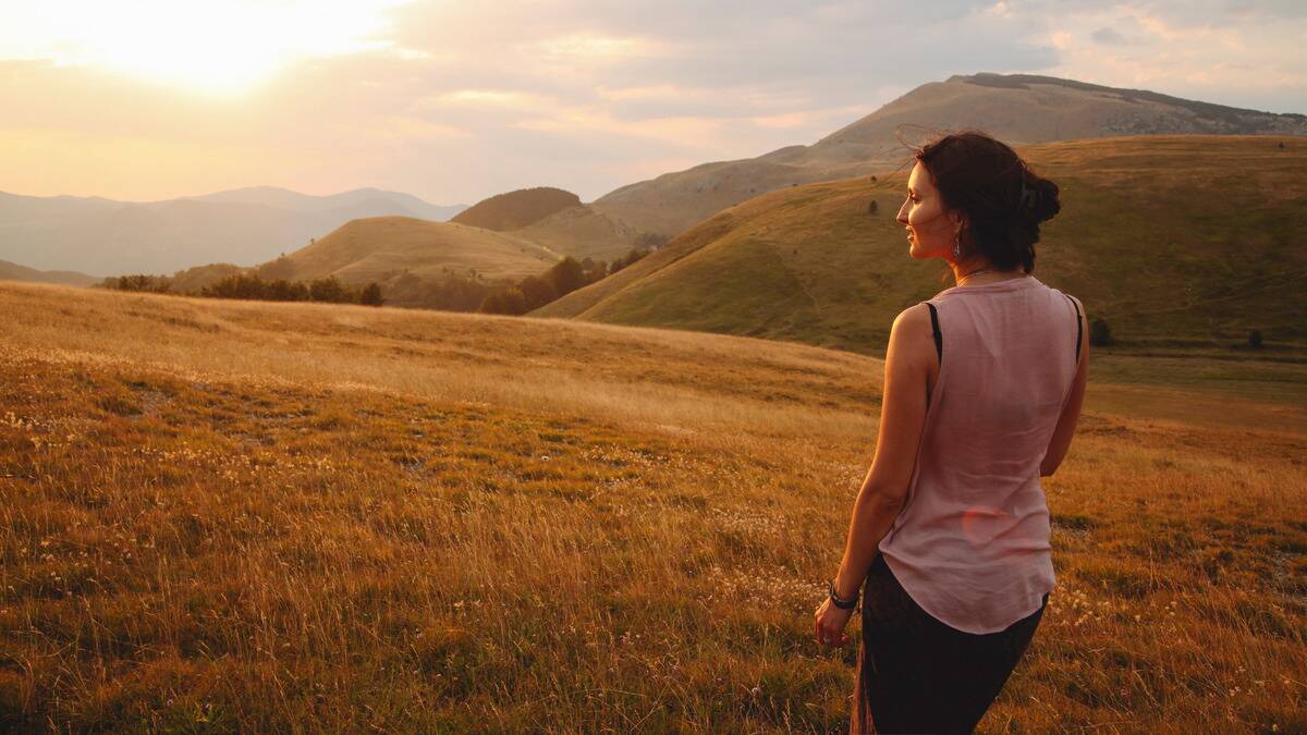 A woman standing in a field, looking out at the rising sun.