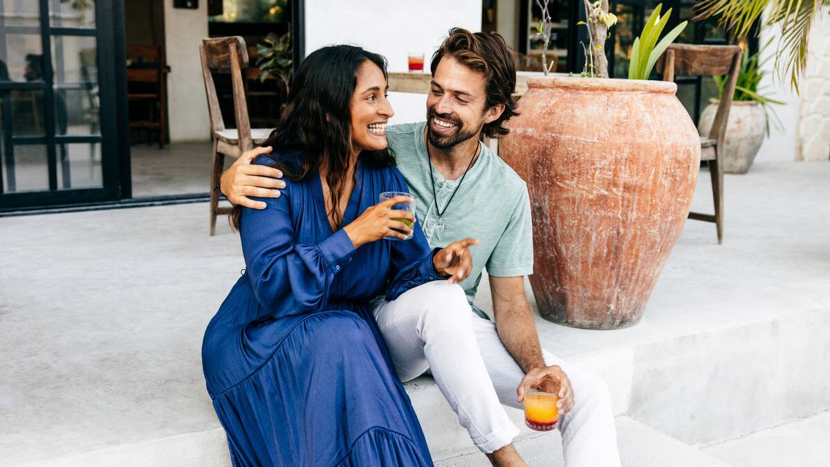 A couple sitting outdoors, the man with his arm around the woman, both holding drinks and smiling.