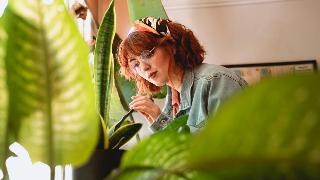 A woman examining a snake plant, framed by other houseplants.