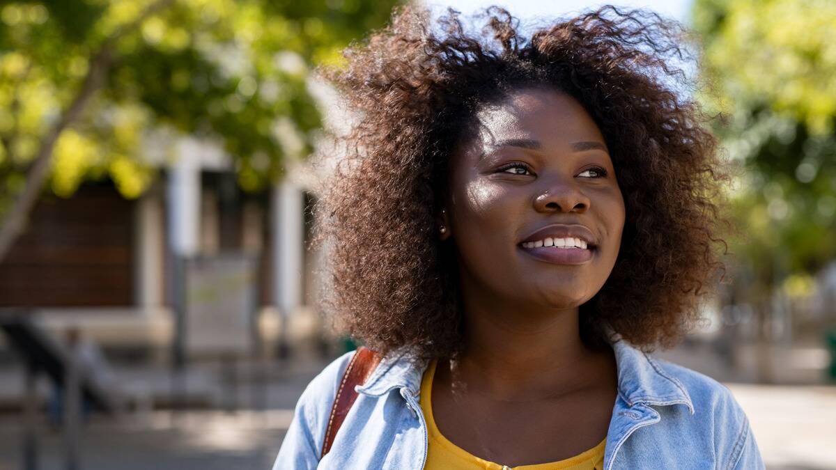 A woman standing outside in the sun, smiling as she looks off to the side.