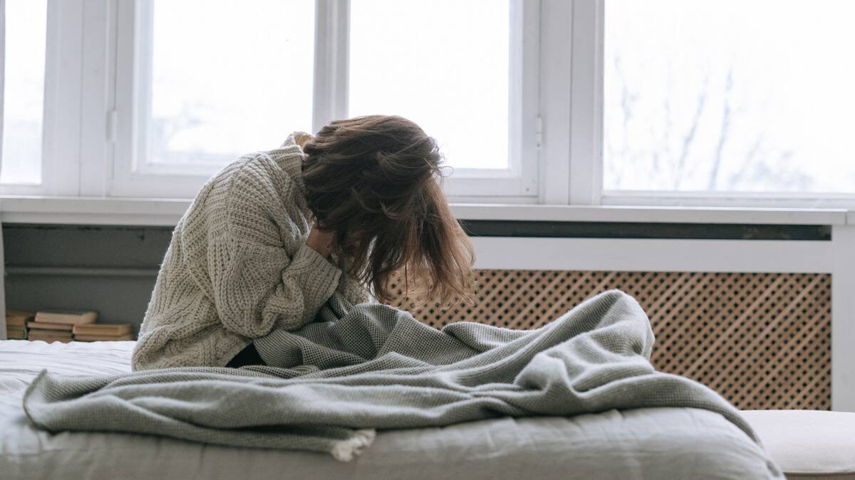 A woman sitting up in bed, leaning forward, head in her hands.