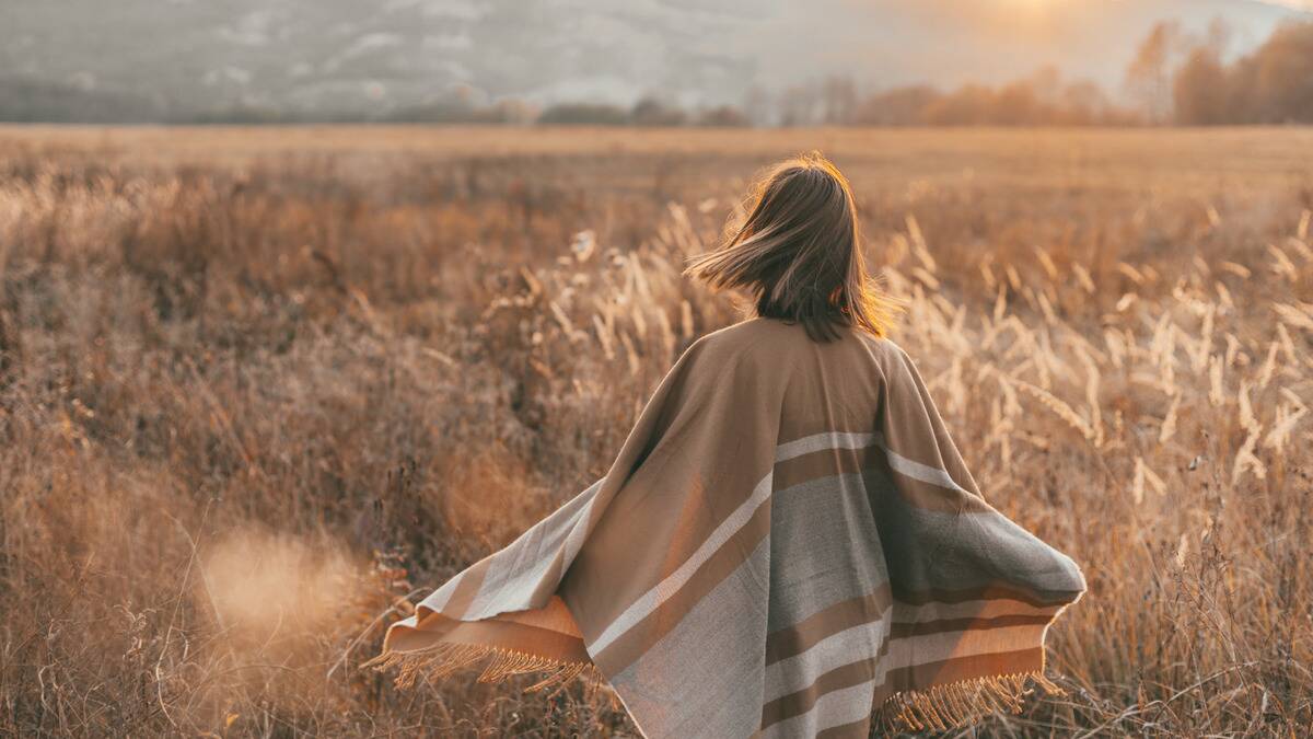 A woman in a poncho standing in a field of tall grass.