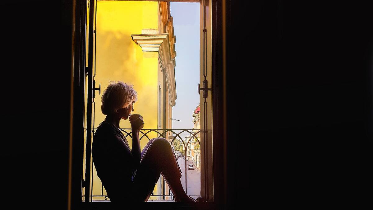 A woman sitting in a windowframe in the morning, sipping from a mug.