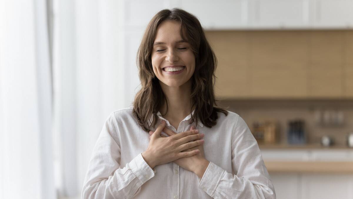 A woman smiling brightly with her eyes closed, both hands over her heart.