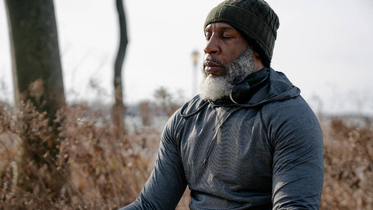 A man sitting outside with his eyes closed, appearing to be meditating.