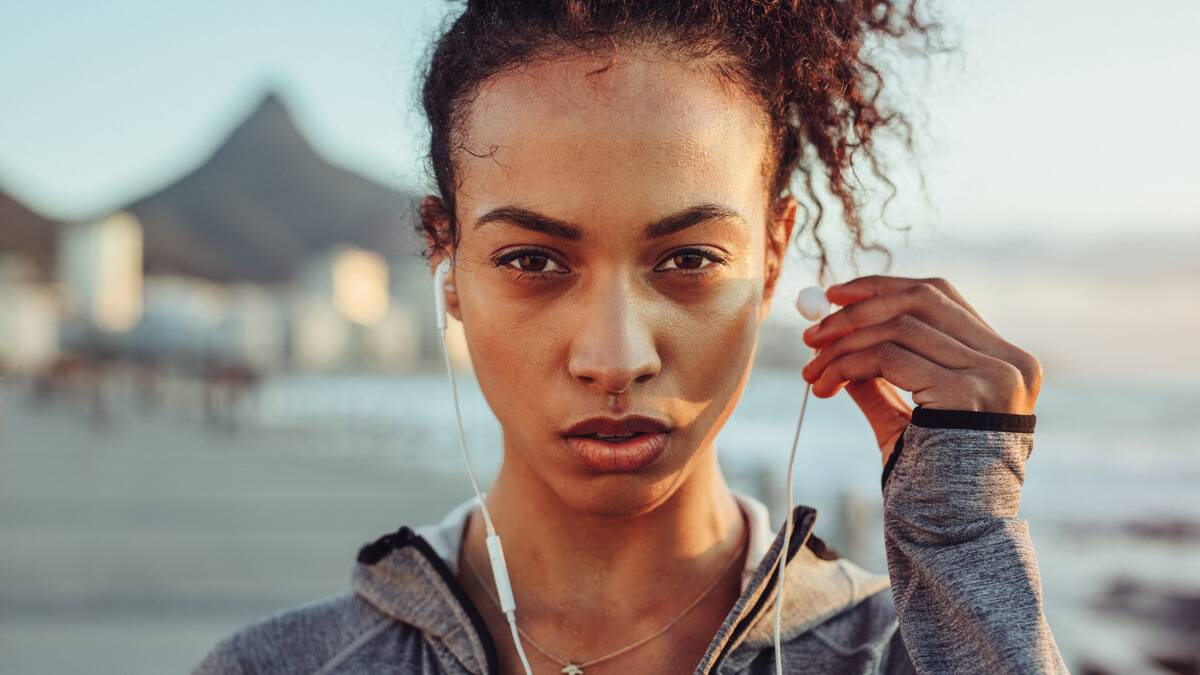 A close, head-on shot of a woman who's looking forward with a determined expression, taking one earbud out of her ear.