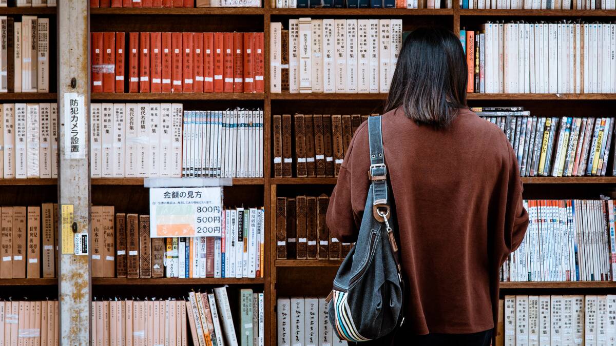 A woman standing in front of a book store shelf browsing the selection.