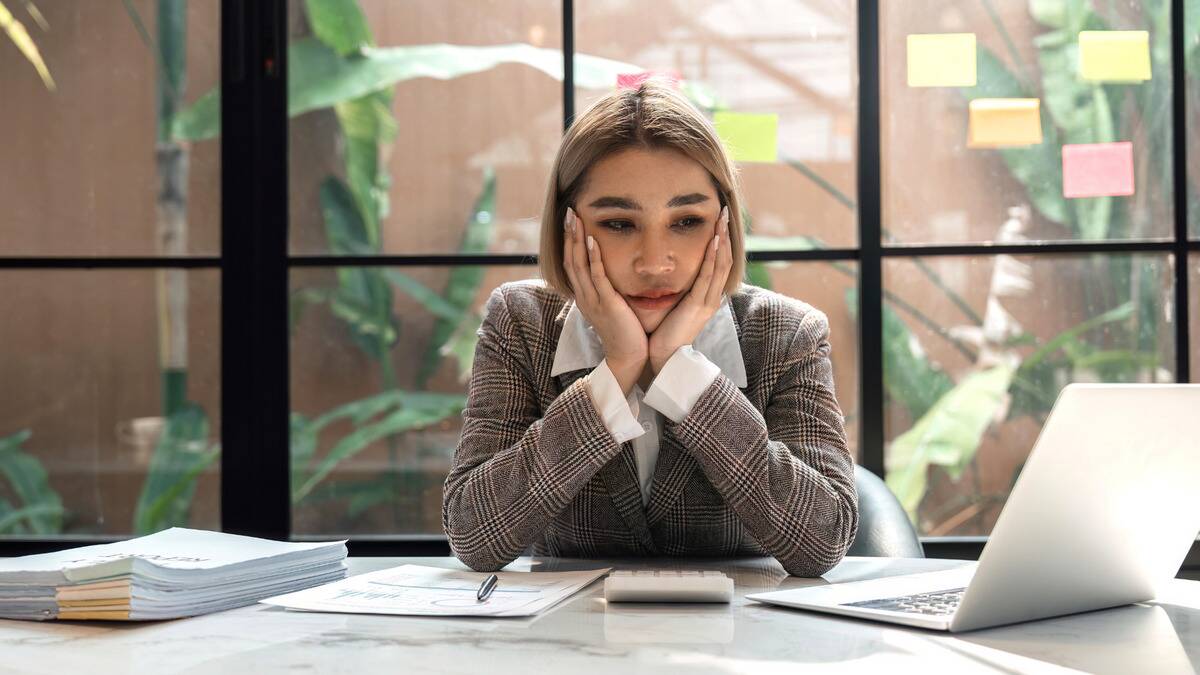 A woman sitting at her desk at work, her chin in both hands, looking dejected.