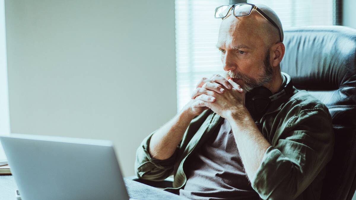 A man sitting at his desk with his arms folded together by his face, looking serious and thoughtful.