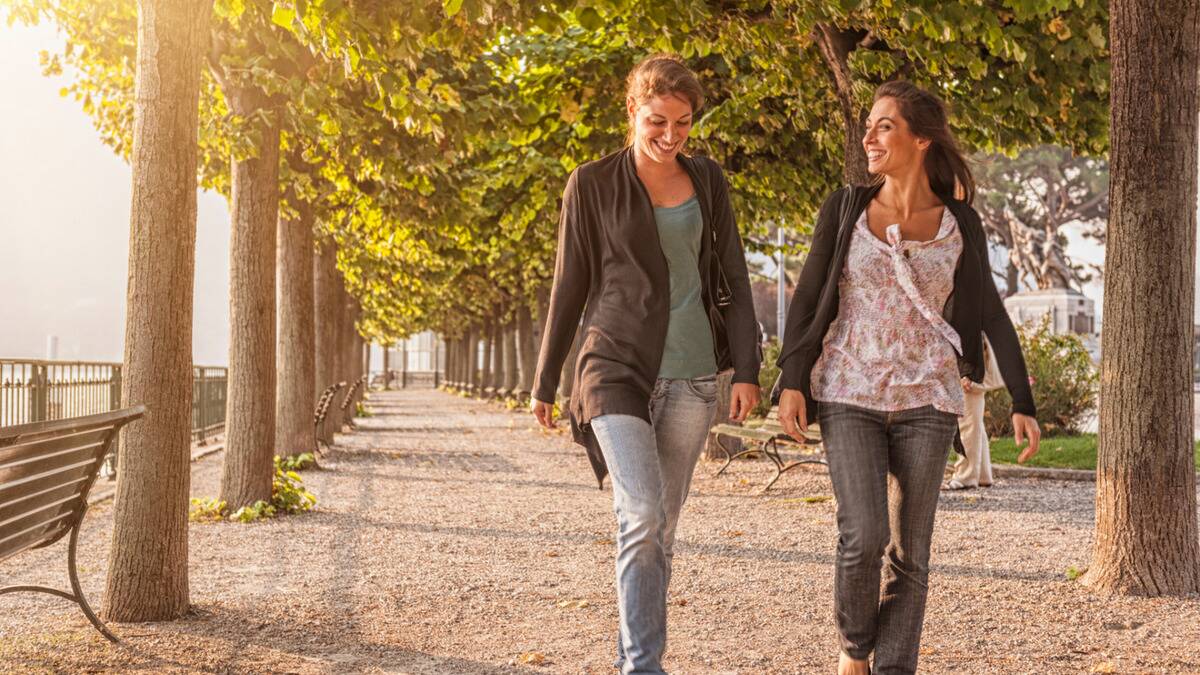 Two friends talking down a path outside, smiling as they chat.