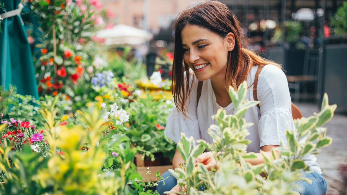 A woman kneeling among some plants, smiling as she browses.