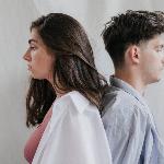 A man and woman standing back to back in front of a white backdrop, both looking melancholic.