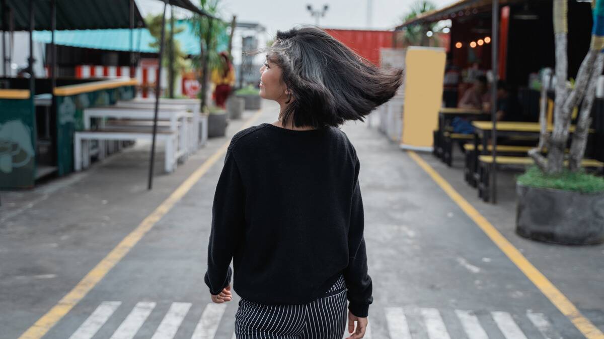 A woman facing away from the camera as she walks down the street, tossing her hair back as she smiles.