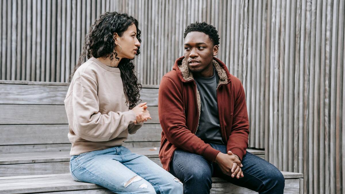 A couple sitting side by side on a bench, looking incredulously at one another.