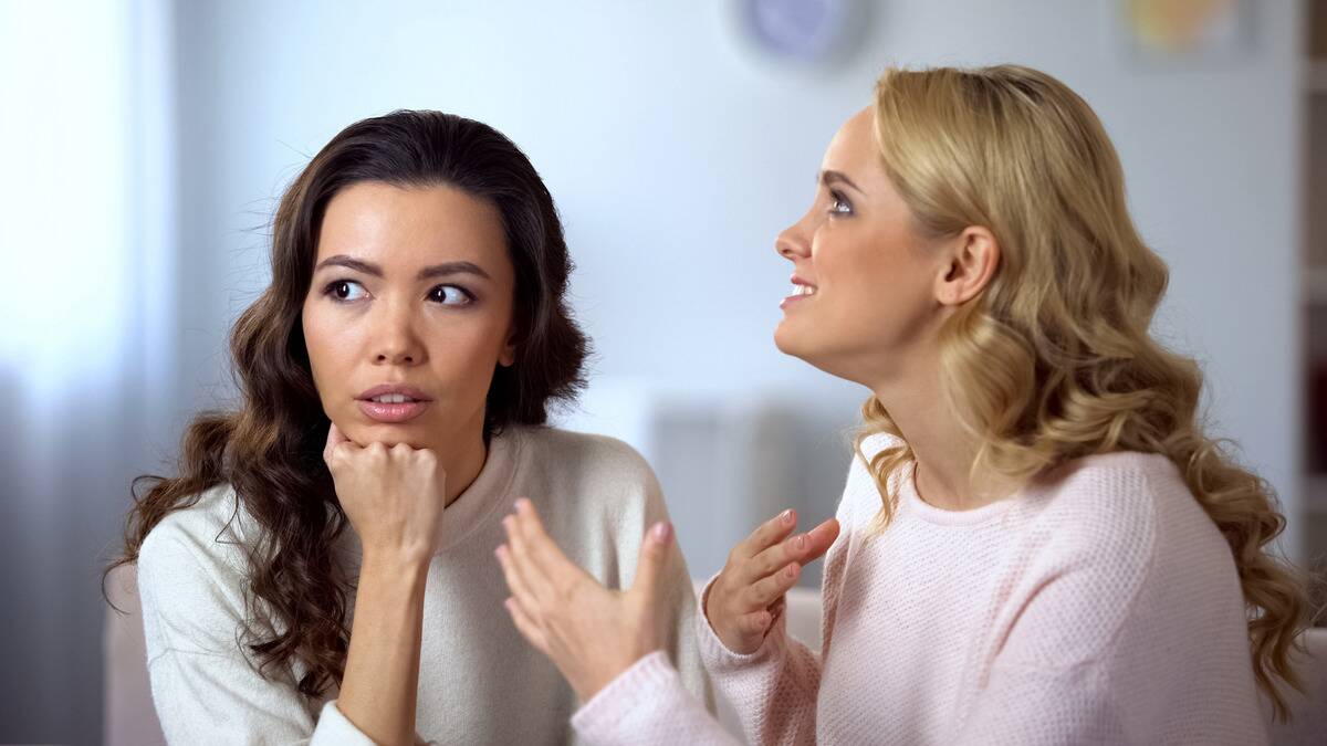 One woman chatting away while another looks to the side, seeming annoyed.