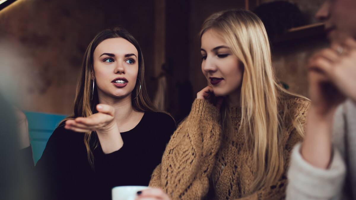 Two friends talking, one animatedly, one looking down, seeming tired.