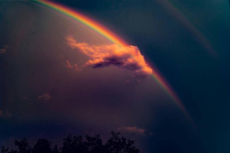 A rainbow streaking behind a cloud that's also hiding the sun, creating a golden glow.