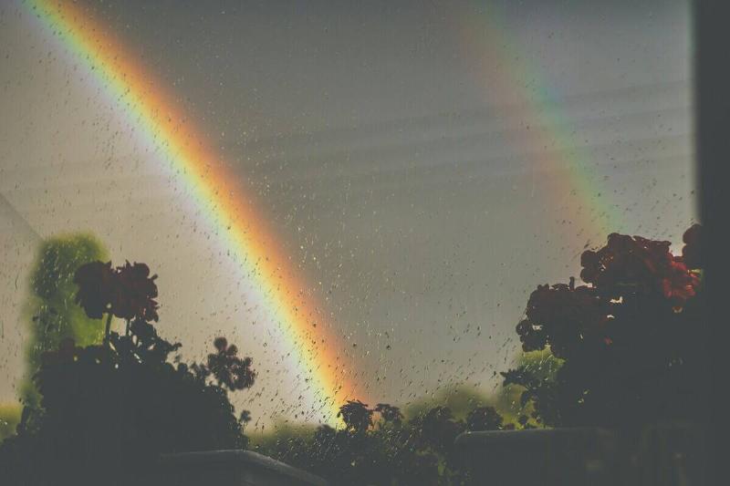 A rainbow seen through a rain-covered window.