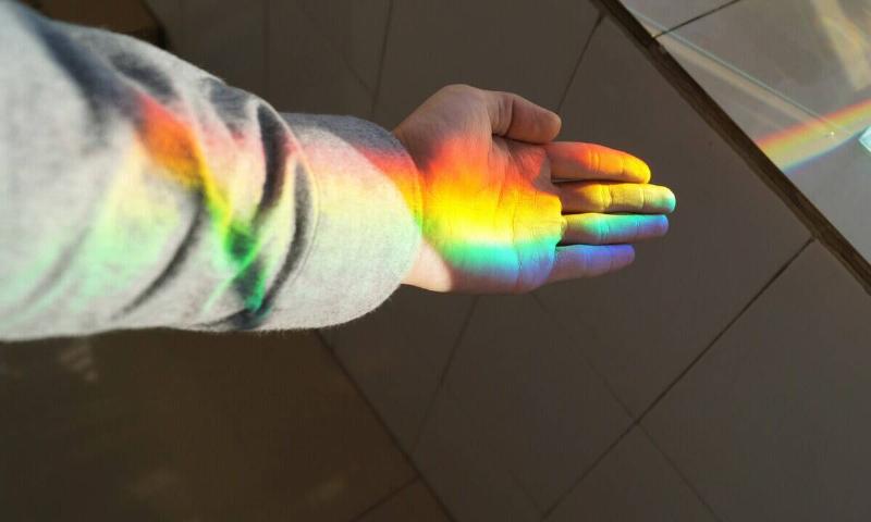 A rainbow shining through a window onto someone's hand and arm.