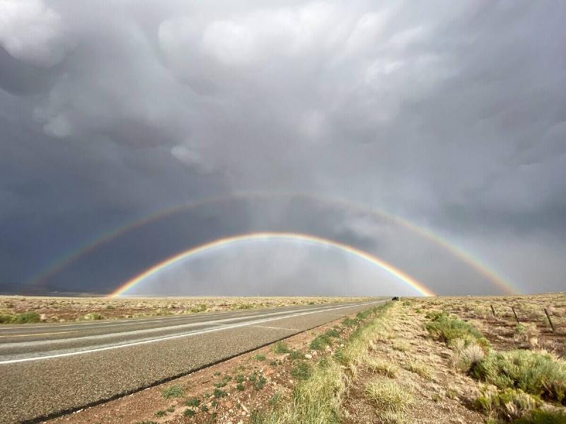 A double rainbow seen in grey skies above a desert road.