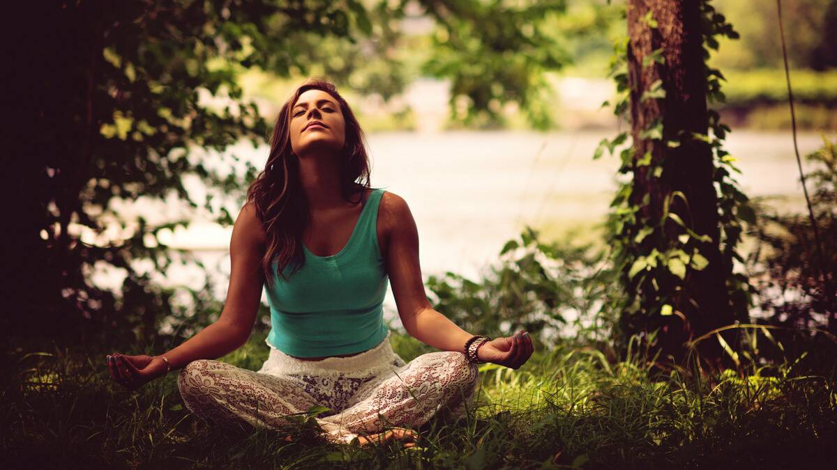 A woman sitting outside meditating, eyes close and head tilted upward.