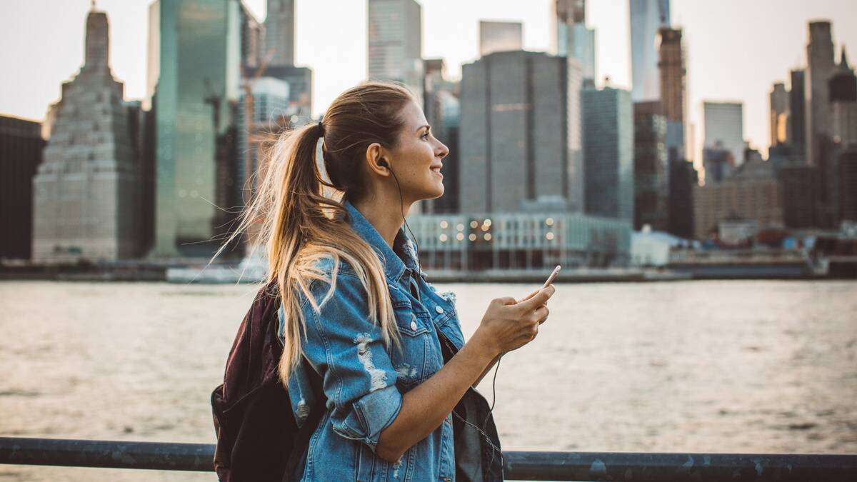 A woman walking through the city, smiling as she looks forward, listening to music on her phone.