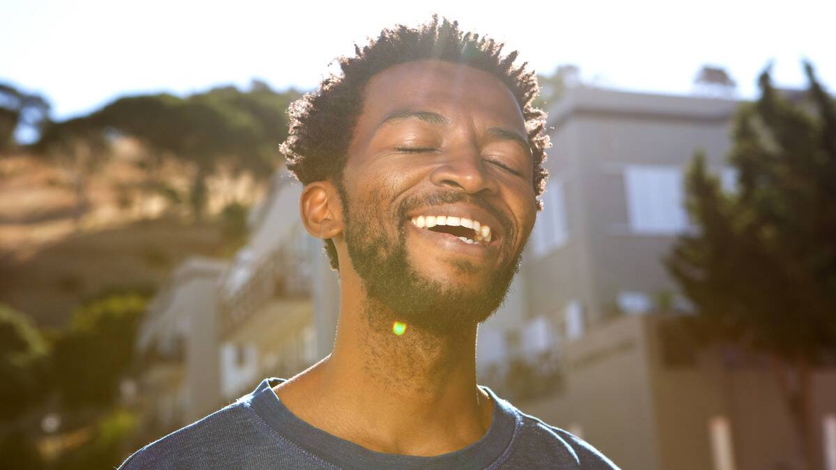 A man with his eyes closed smiling as he walks outside in the sun.