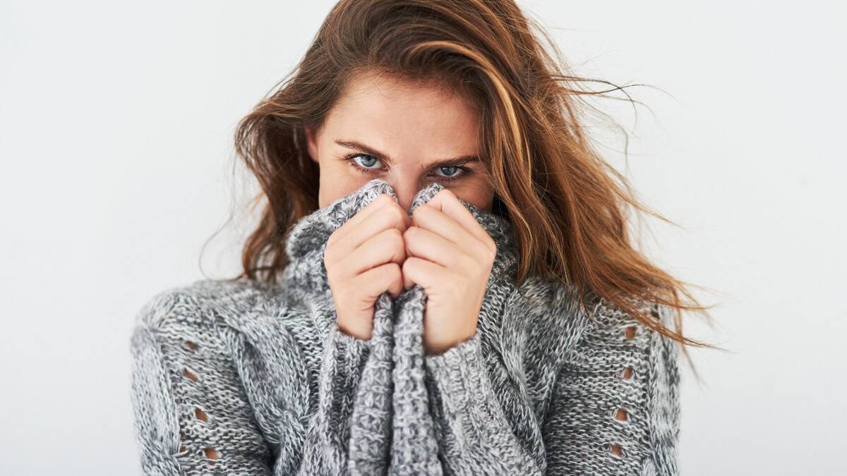 A woman wearing a large, cozy sweater, lifting it to cover the bottom half of her face.