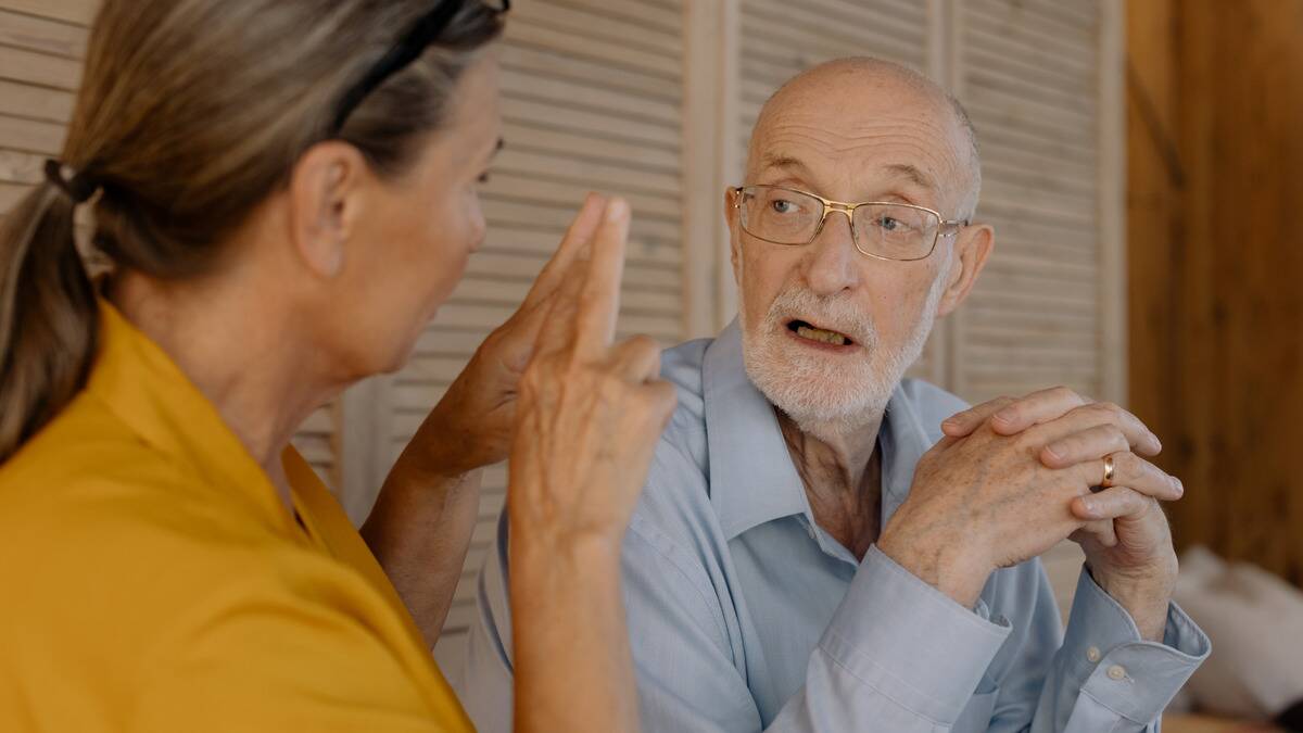 A woman speaking to an older man who looks confused at what she's gesturing.