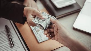 A folded $100 bill being passed hands across a desk.