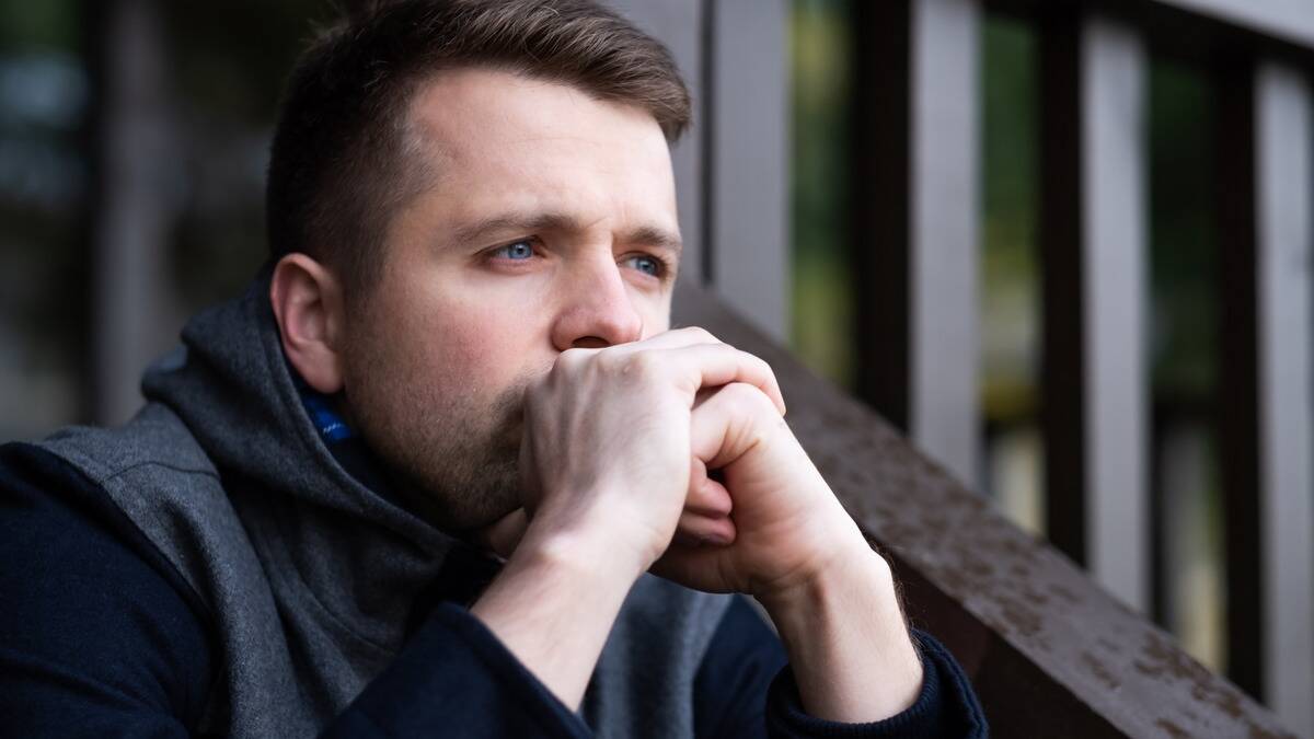 A man sitting on a stoop outside with his hands to his mouth, looking concerned.