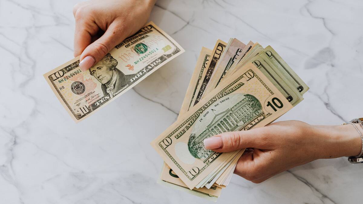 An above shot of a pair of hands counting a stack of $10 bills.