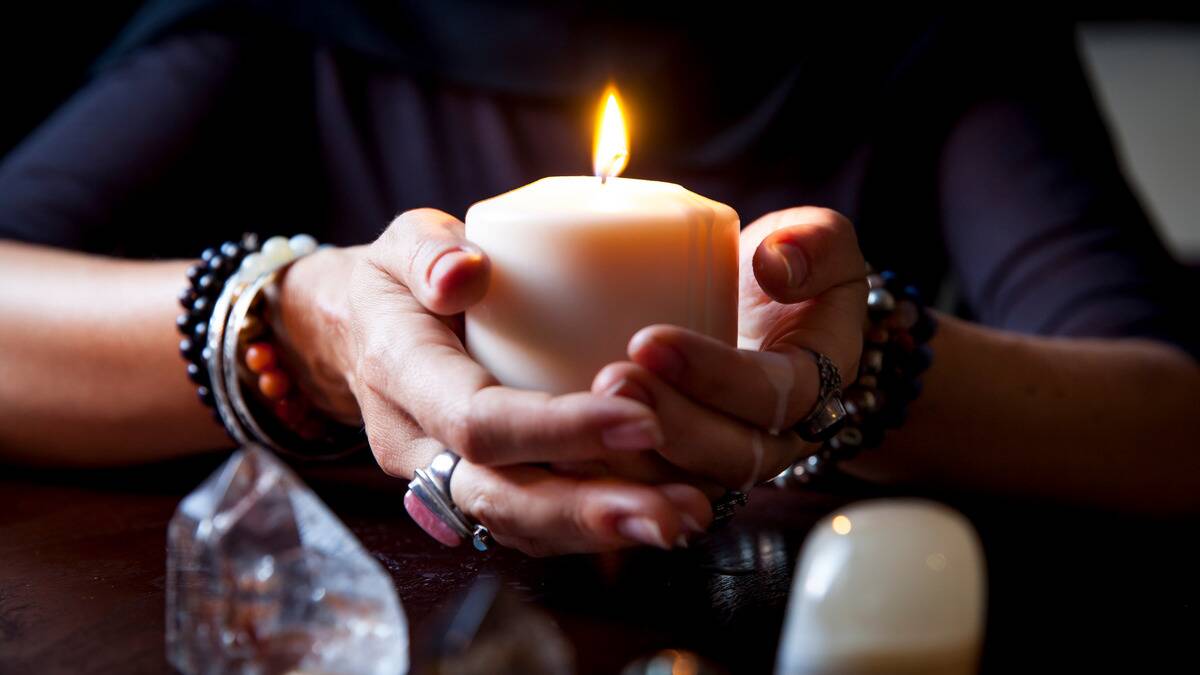 A close photo of a woman's cupped hands holding a large, lit candle.