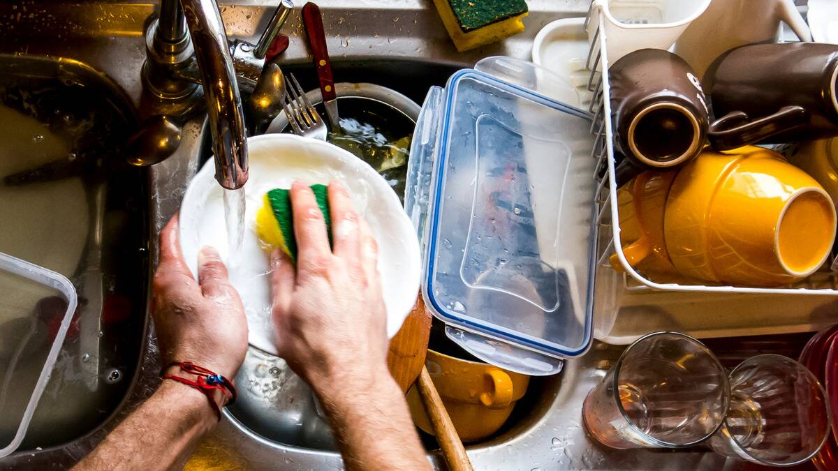 A POV shot of someone washing dishes atop their full sink.