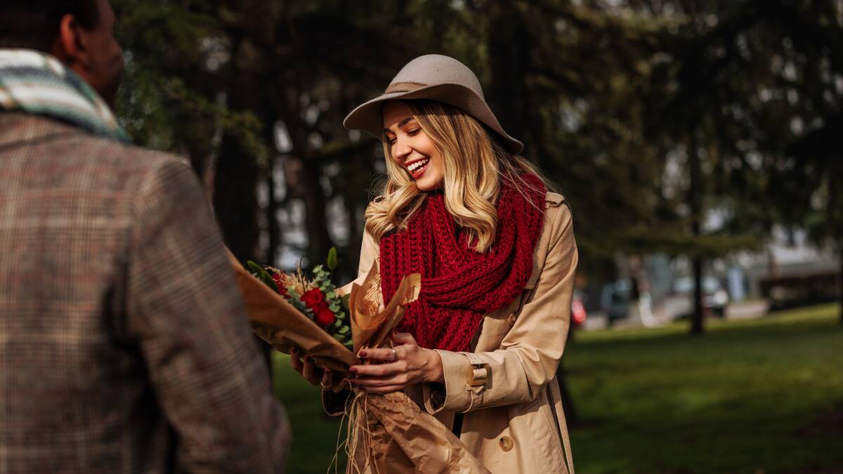 A woman smiling as she holds and looks at a bouquet she was just given by a man who's mostly out of frame.