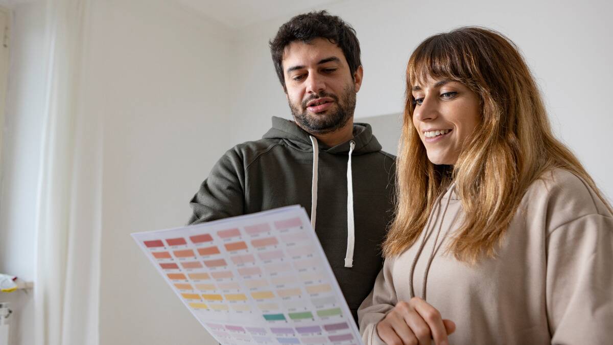 A couple standing in a bare room of their home, looking at paint colors together.