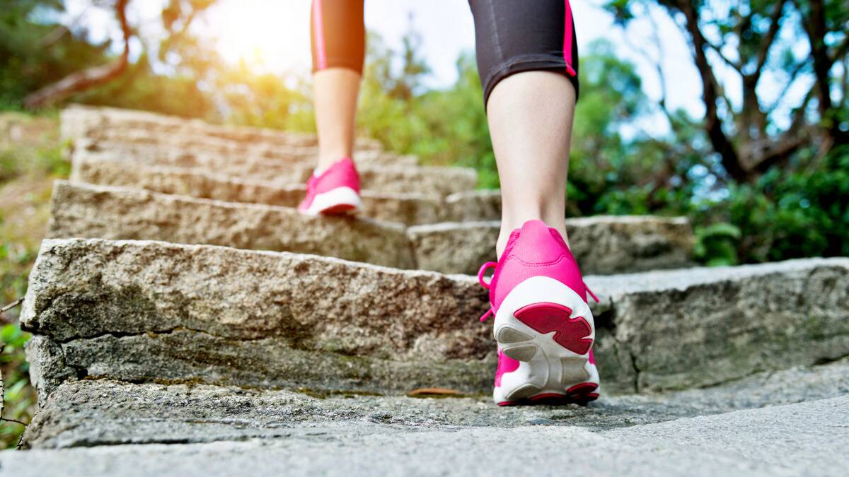 A close, low photo of a woman's bright pink running shoes taking a step up a stone outdoor staircase.