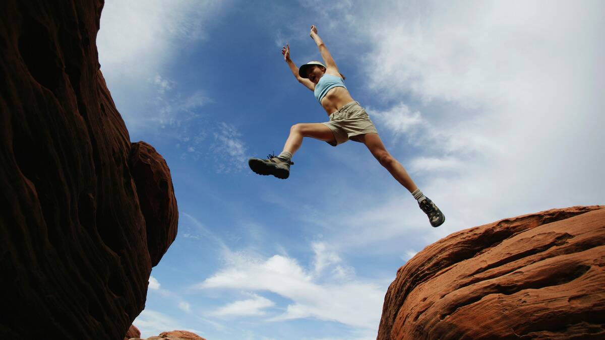 A low-angle shot of a woman leaping across two rocks.