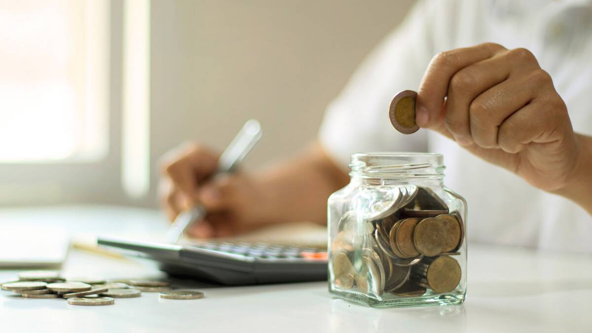 Someone writing out some calculations while they count coins and place them in a jar.