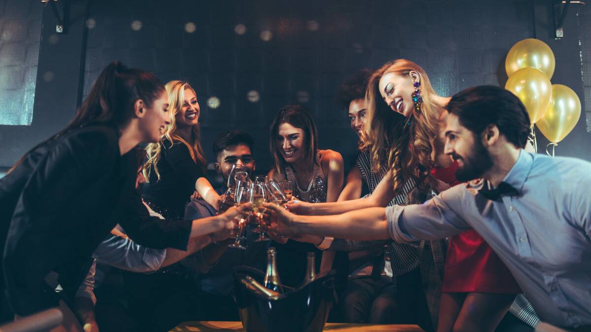 A group of friends at a bar all cheers'ing glasses of champagne together.