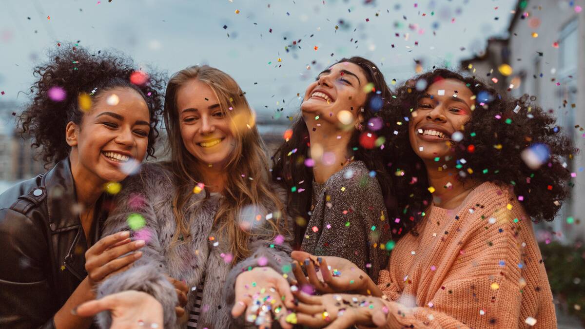 Four friends standing side by side, smiling as confetti rains around them.