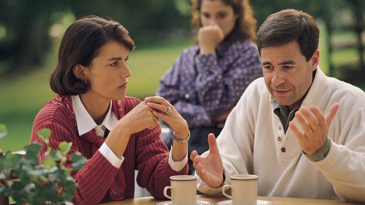 A man and woman speaking at a table, both looking concerned.