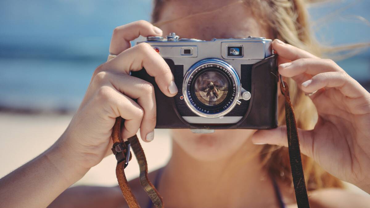 A woman holding a film camera up to her face.