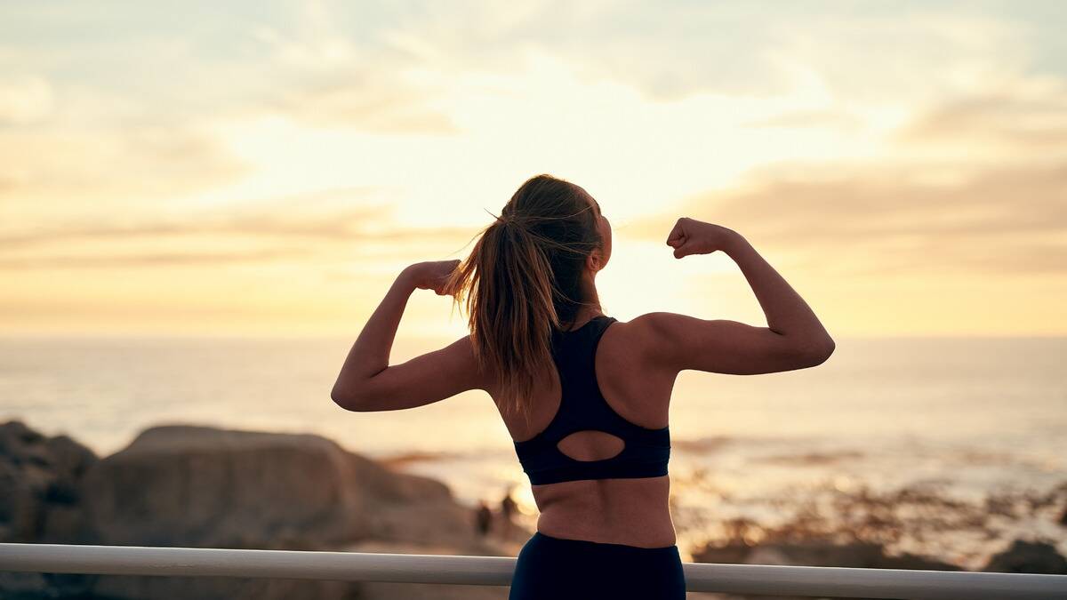 A woman flexing her arms as she stands before the rising sun.