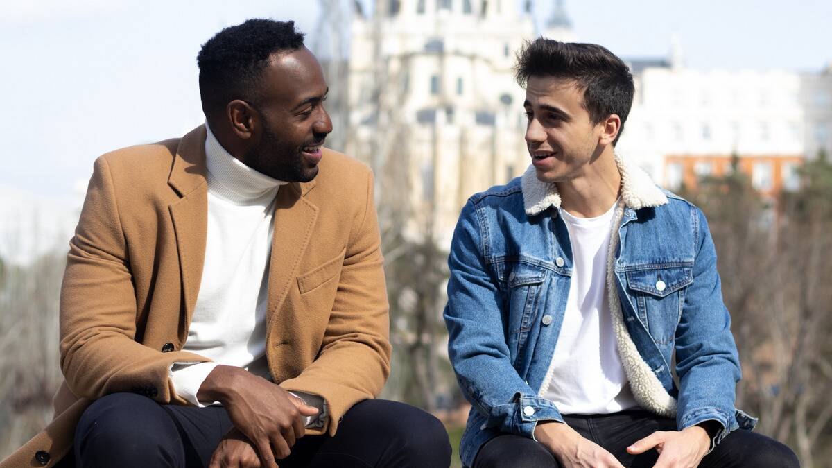 Two friends sitting side by side outdoors, smiling at one another as they talk.