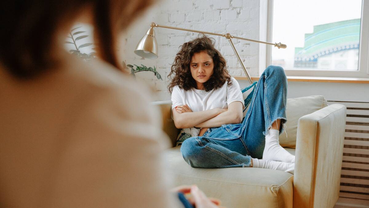 A young woman glaring angrily with her arms crossed at a therapist whose shoulder we're looking over.