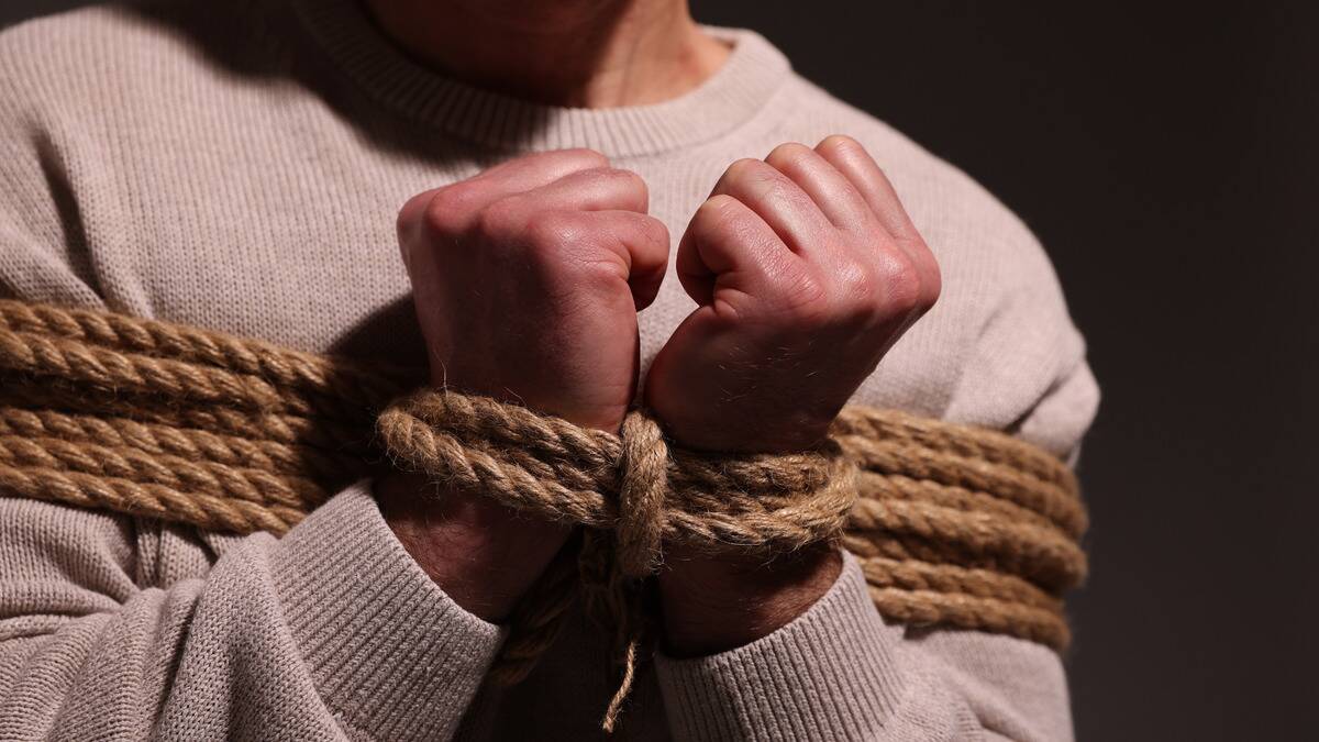 A close photo of someone's hands closed into fists as their wrists are tired to their chest using thick rope.